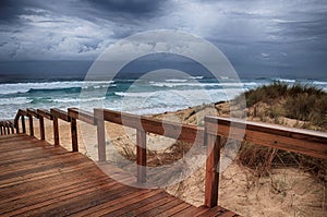 Wooden pathway on the beach by the breathtaking ocean waves under the cloudy sky