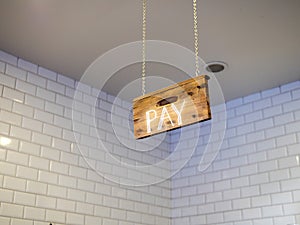 Wooden pay sign hanging over cash register payment area in cafe