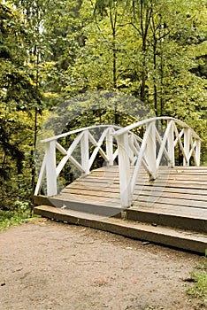 Wooden pedestrian bridge across a small river in an old park in Russia.