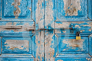 Wooden peeled blue door, closed, locked, aged for background. Rusty latch and padlock. Close up view.