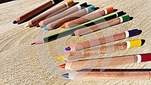 Wooden pencils of different colors lie on a beige table. Among them stands out one longer graphite pencil. Dissimilarity,