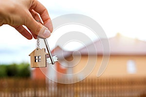 Wooden pendant of a house and key. Background of fence and cottage. Dream of home, building, design, delivery of the project, movi