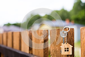 Wooden pendant of a house and key. Background of fence and cottage. Dream of home, building, design, delivery of the project, movi