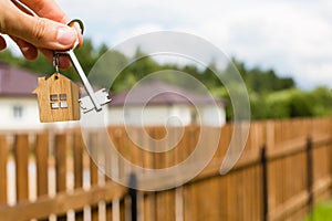 Wooden pendant of a house and key. Background of fence and cottage. Dream of home, building, design, delivery of the project, movi