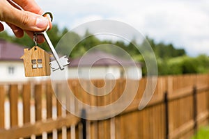 Wooden pendant of a house and key. Background of fence and cottage. Dream of home, building, design, delivery of the project, movi photo
