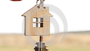 Wooden pendant of a house and key in hand. Background of the sky and field. Dream of home, building a cottage in the countryside,