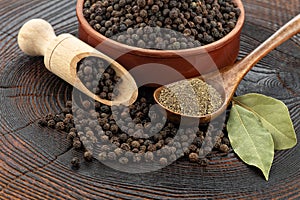 Wooden pepper mill, black peppercorns, ground black pepper and laurel leaves on old wooden table