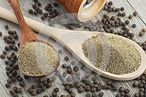 Wooden pepper mill, black peppercorns and ground black pepper on old wooden table