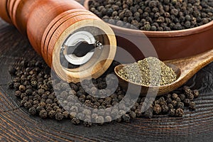 Wooden pepper mill, black peppercorns and ground black pepper on old wooden table