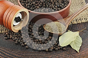 Wooden pepper mill, laurel leaves, black peppercorns and ground black pepper on old wooden table