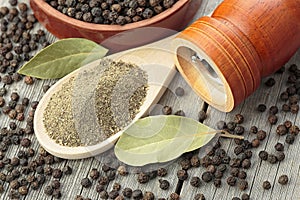 Wooden pepper mill, laurel leaves, black peppercorns and ground black pepper on old wooden table