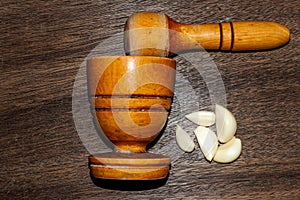 wooden pestle and mortar with garlic cloves on a textured senital
