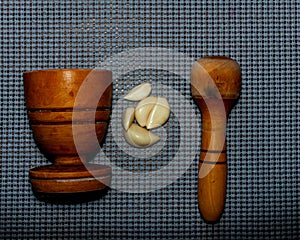 wooden pestle and mortar with garlic cloves on a textured