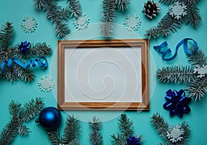 Wooden photo frame, fir branches, white snowflakes, blue balls, cones and serpentine on a light blue background.