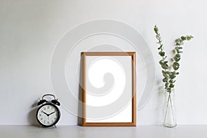 A wooden photo frame with green leave and clock on table with natural light.