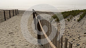 Wooden picket fence, sandy misty beach, California USA. Pacific ocean coast, fog haze on sea shore.