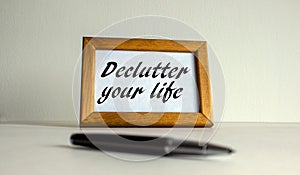 Wooden picture frame with inscription `declutter your life` on beautiful white fon. Pen on the table