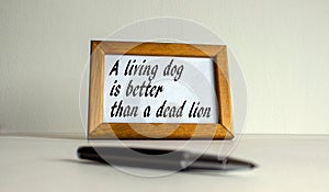 Wooden picture frame with inscription `a living dog better than a died lion` on beautiful white fon. Pen on the table