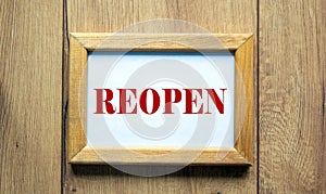 Wooden picture frame with inscription `reopen` on beautiful wooden background. Concept