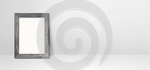Wooden picture frame leaning on a white wall. Horizontal banner