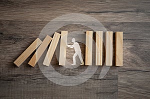 Wooden pieces with stick figure metaphor for stopping domino effect on wooden background