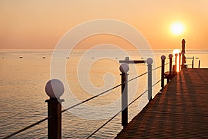 Wooden pier on the beach against the background of the orange sky and the rising sun