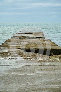 Wooden pier on the beach. Sunset and calm ocean. Calm. Stone beach of cold sea.