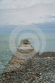 Wooden pier on the beach. Sunset and calm ocean. Calm. Stone beach of cold sea.