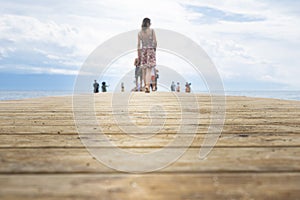 Wooden pier. Boardwalk at sea shore with beautiful woman and people in the distance. Focus on the wooden boards