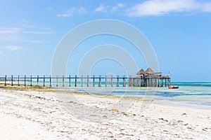Wooden pier with boat and beach hut. Low tide of Indian Ocean. Idyllic exotic resort. Pier in perspective with bungalow.