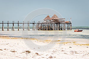 Wooden pier with boat and beach hut. Low tide of Indian Ocean. Idyllic exotic resort. Pier in perspective with bungalow.