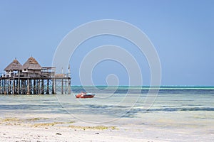 Wooden pier with boat and beach hut. Low tide of Indian Ocean. Idyllic exotic resort. Pier in perspective with bungalow.