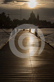 Wooden pier with boats at sunset in Amsterdam dock. Amsterdam city silhouettes in evening dusk light.