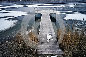 Wooden pier on frozen lake on winter, snow and brown grass