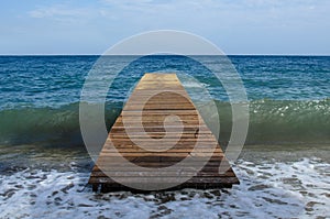 Wooden pier on the infinite sea without anyone under it passes a wave that breaks on the shore