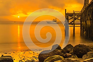 Wooden pier juts out into calm body of water, bathed in golden light of sunrise in Banyuwangi.