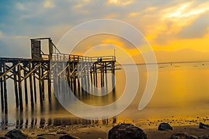 Wooden pier juts out into calm body of water, bathed in golden light of sunrise in Banyuwangi.