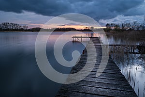 Wooden pier on the lake at cloudy sunset, view on a spring evening