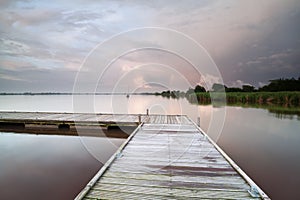 Wooden pier on lake during shower at sunset