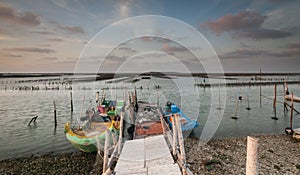 Wooden pier by a lake with two boats next to it with the beautiful cloudy sky in the background