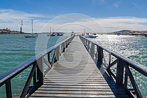Wooden pier leading out into bay on sunny day with many boats, Luderitz, Namibia, Southern Africa