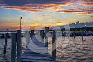 A wooden pier leading to a lake on Lake Neusiedl in Podersdorf, Austria. In the background is a dramatic sky at sunrise