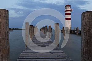 A wooden pier leading to the lake and a red and white lighthouse on Lake Neusiedl in Podersdorf, Austria. In the background is a