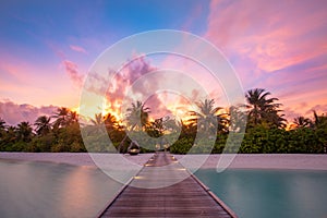 Wooden pier with lights into paradise island in Maldives. Sunset beach landscape, exotic travel vacation destination, summer shore