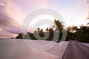 Wooden pier with lights into paradise island in Maldives. Sunset beach landscape, high key bright sky calm sea water