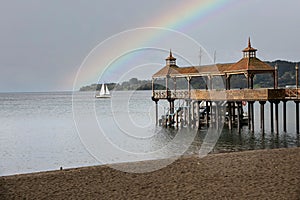 Wooden pier on the Llanquihue lake under a gloomy sky with a rainbow in Frutillar, Chile