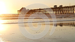 Wooden pier on piles, silhouette at sunset, California USA, Oceanside. Sunny sea waves at sundown.