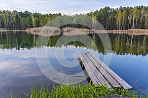 Wooden pier and spring forest on a calm lake in Ukraine. Nature and travel concept