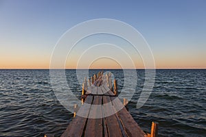 Wooden pier at the sunset. Evening sky over sea with footbridge. Calm evening landscape. Empty pier at seaside with copy scape.