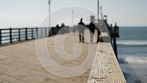 Wooden pier waterfront boardwalk, California beach USA. Defocused ocean, sea waves. People walking.